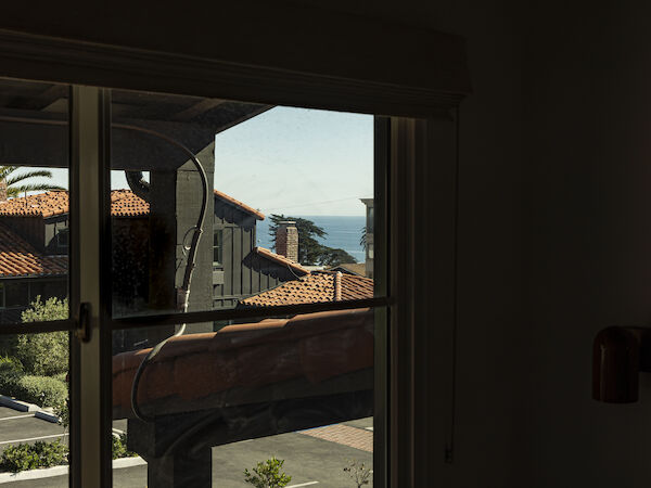 A view through a window shows rooftops, a street, and a glimpse of the ocean beyond, with bright daylight outside.