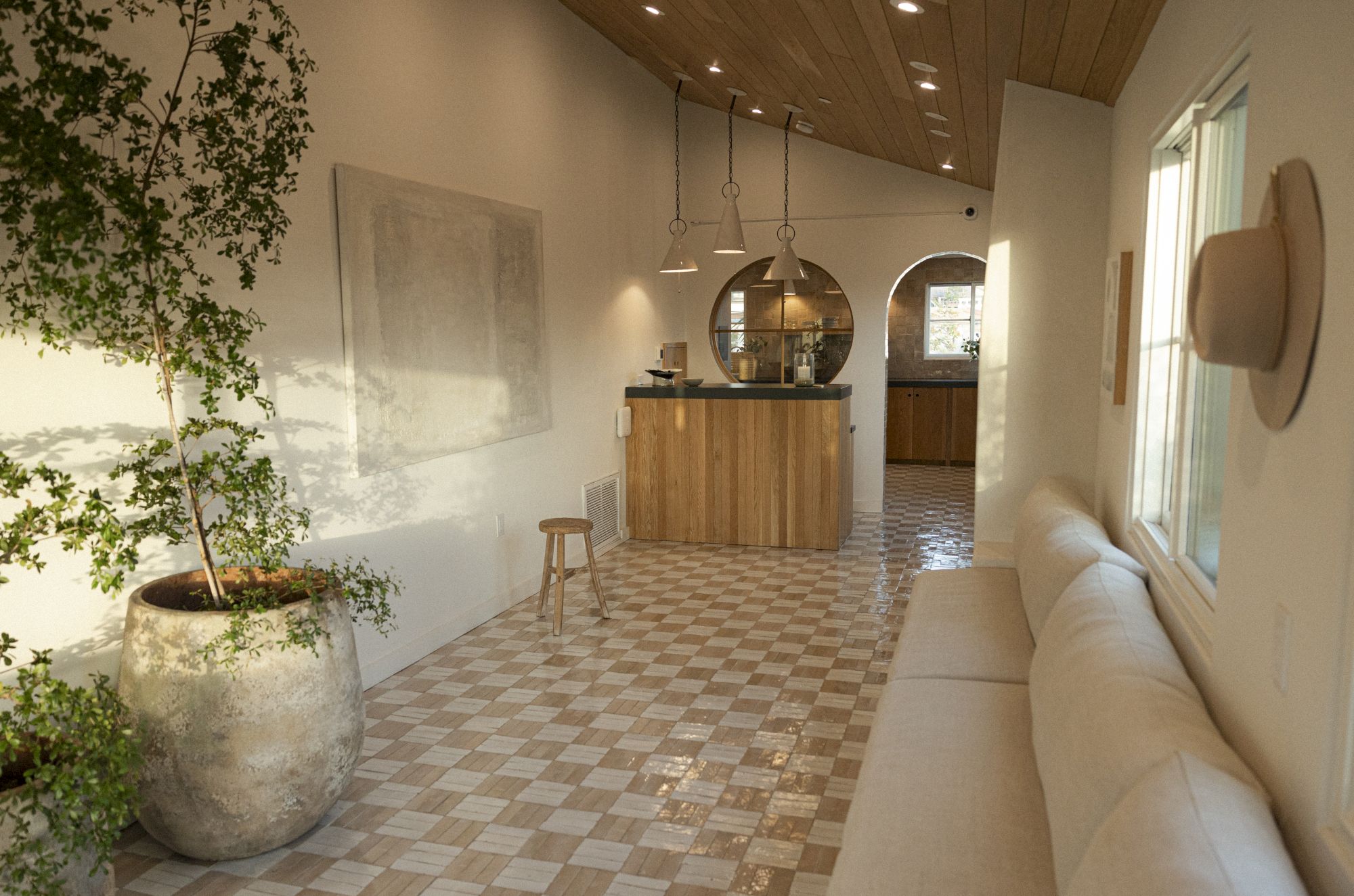 A bright, airy lobby with tiled checkered floor, potted plant, wooden reception desk, bench seating, and modern light fixtures. End sentence.