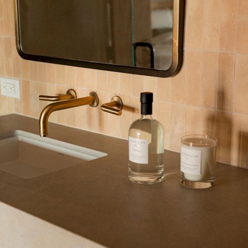 A bathroom counter with a sink, soap dispenser, bottle, and a towel; a large mirror hangs above.