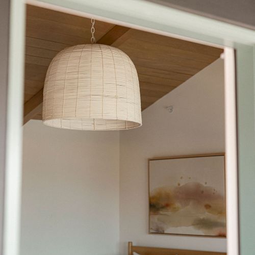 A hanging woven lampshade above a bed in a cozy, minimalist bedroom.