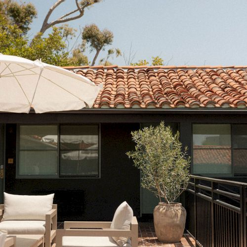 A rooftop terrace with outdoor seating, a potted plant, and a brick wall; clear sky above.