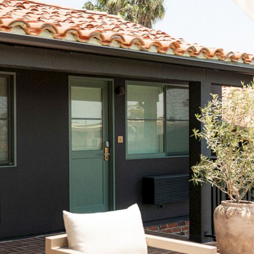 A modern outdoor seating area with a beige chair, glass doors, desert-style landscaping, and a clay-tiled roof patio.