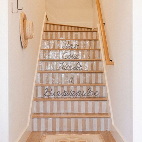 A wooden staircase with a wicker-looking mesh gate, narrow hallway, warm lighting, and a small rug at the top, ending with a closed wooden door.