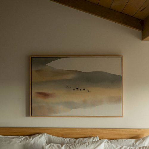 A wooden boat model or sculpture with a pale, weathered banner or rope on a shelf against a plain wall, small framed item in the background.