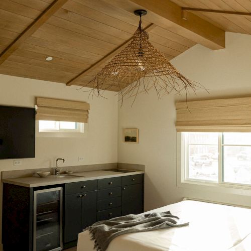 A kitchen and dining area with a ceiling fan, light wood cabinets, a dark countertop, and a bright windowed wall.