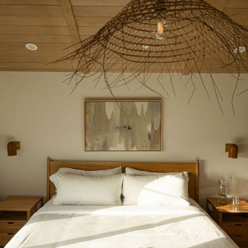 A cozy bedroom with a wooden ceiling, warm lighting, a large bed, and framed artwork above the headboard, creating a rustic, inviting vibe.