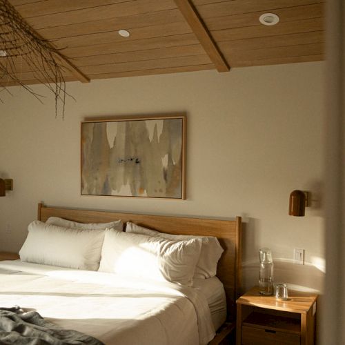 A cozy hotel bedroom with a double bed, warm lighting, a wooden headboard, framed art, and a small nightstand &mdash; simple, inviting.