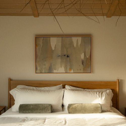 A cozy bedroom with a wooden bed, two pillows, a framed wall art above, and soft lighting in a warm-toned room.