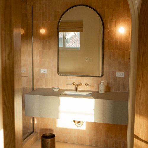 A cozy hallway leads to a warmly lit arched mirror and doorway, with a small table and plants along the wall, creating a welcoming entry.