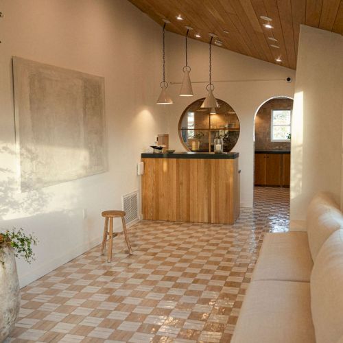 A bright hallway leading to a cozy living area with warm wood tones, potted plants, and soft lighting at the end.