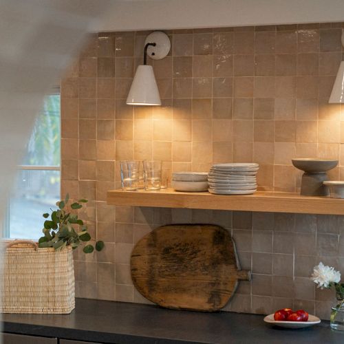 A cozy wall shelf with warm lighting, ceramics, and plants in a rustic alcove.