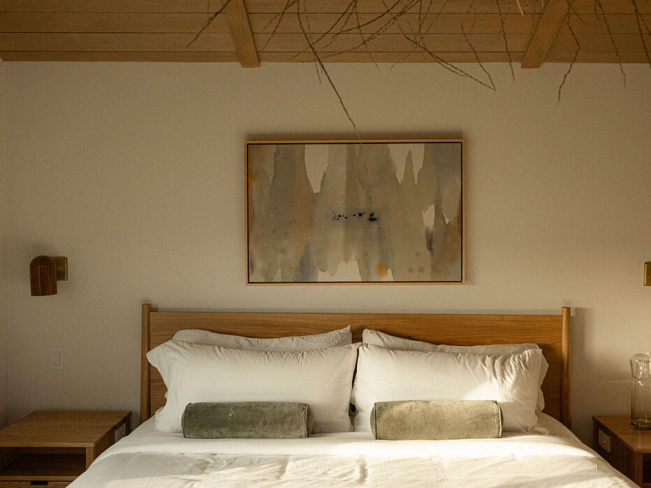 A cozy bedroom with a wooden bed, white bedding, gray pillows, framed wall art, and bedside lamps.