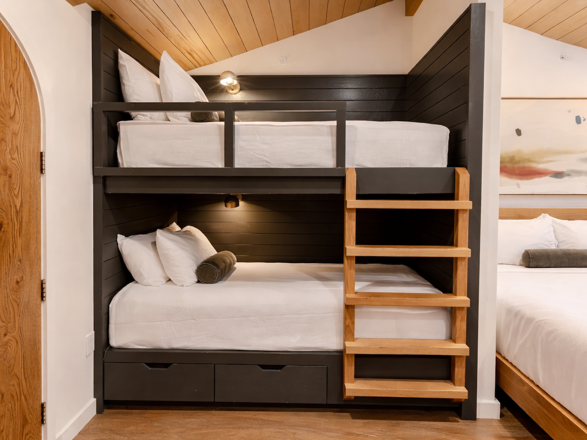A modern bedroom with built-in bunk beds, white bedding, and a spotlight reading lamp on a dark wood frame.