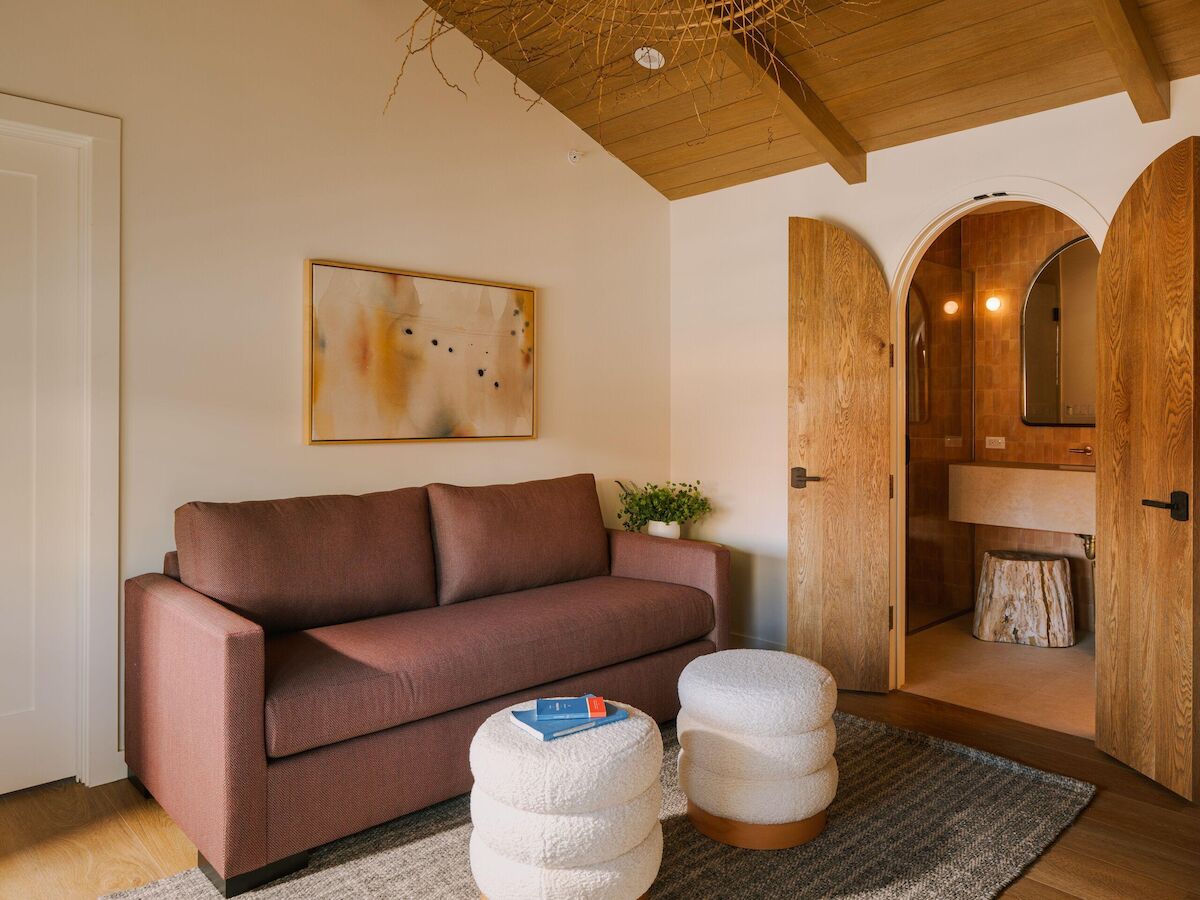 A cozy living room with a brown sofa, framed art, arched wood doorways, and a wooden ceiling above a small spa area.