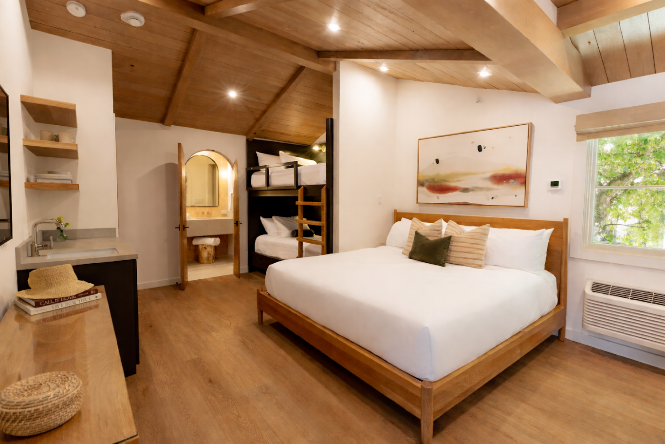 Bright modern bedroom with a wooden vaulted ceiling, large bed, bunk-style storage, window, and framed abstract art on the wall.