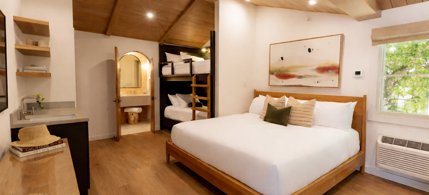 Bright modern bedroom with a wooden vaulted ceiling, large bed, bunk-style storage, window, and framed abstract art on the wall.