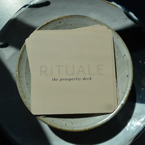 A &ldquo;RITUAL&rdquo; prosperity tarot deck rests on ceramic plates, with the words &ldquo;the prosperity deck&rdquo; visible on the box.
